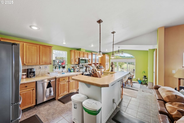 kitchen with light tile patterned floors, a breakfast bar, appliances with stainless steel finishes, an island with sink, and decorative light fixtures