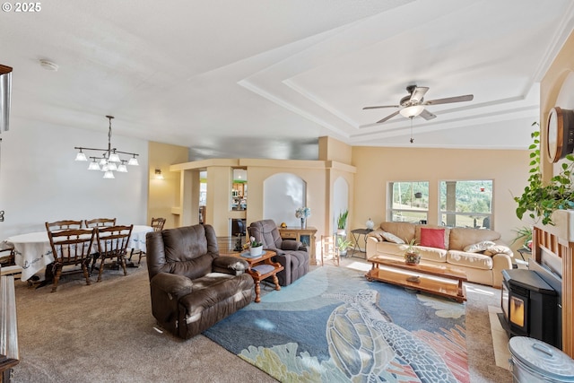 carpeted living room featuring a raised ceiling, a wood stove, and ceiling fan with notable chandelier