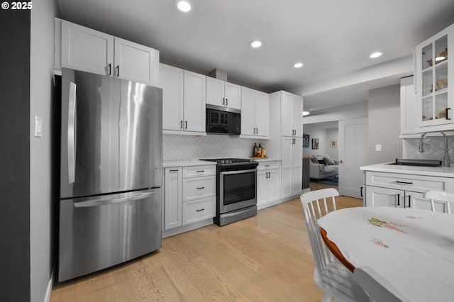 kitchen featuring stainless steel appliances, light countertops, white cabinets, glass insert cabinets, and light wood-type flooring