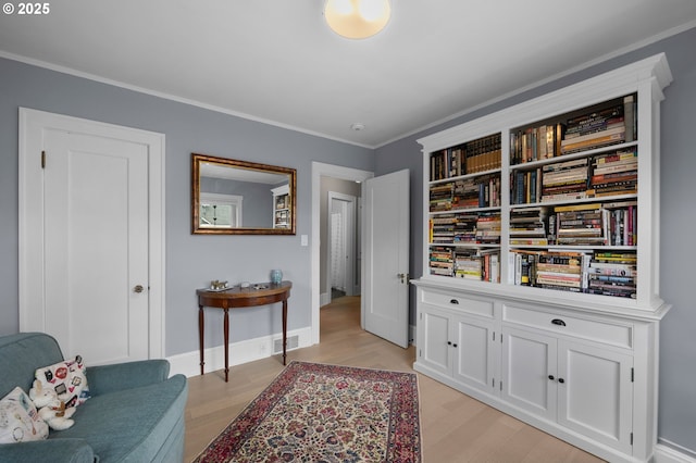 living area with light wood finished floors, visible vents, crown molding, and baseboards