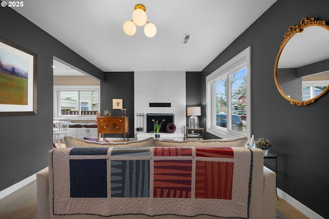 living room with visible vents, a brick fireplace, baseboards, and wood finished floors