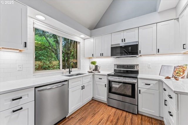 kitchen featuring white cabinets, lofted ceiling, stainless steel appliances, light countertops, and a sink