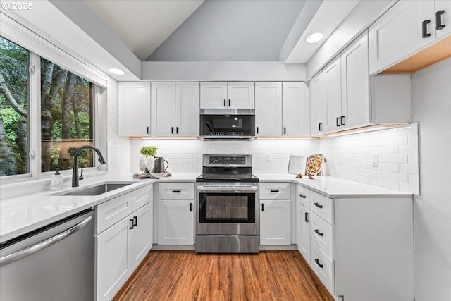 kitchen with a sink, light wood-style floors, stainless steel appliances, white cabinets, and lofted ceiling