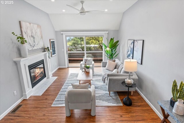 living area with vaulted ceiling, a fireplace with flush hearth, ceiling fan, baseboards, and visible vents