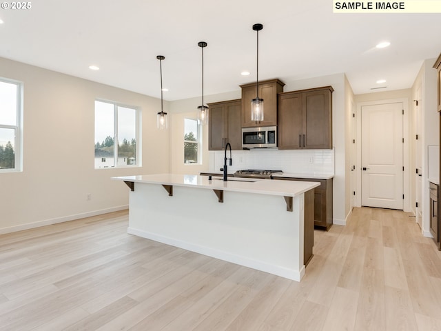 kitchen with light wood-style flooring, light countertops, stainless steel microwave, a kitchen breakfast bar, and tasteful backsplash