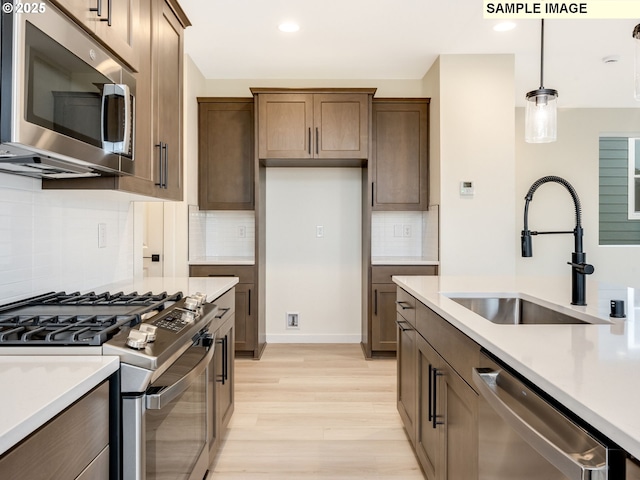 kitchen featuring a sink, appliances with stainless steel finishes, light wood finished floors, light countertops, and hanging light fixtures