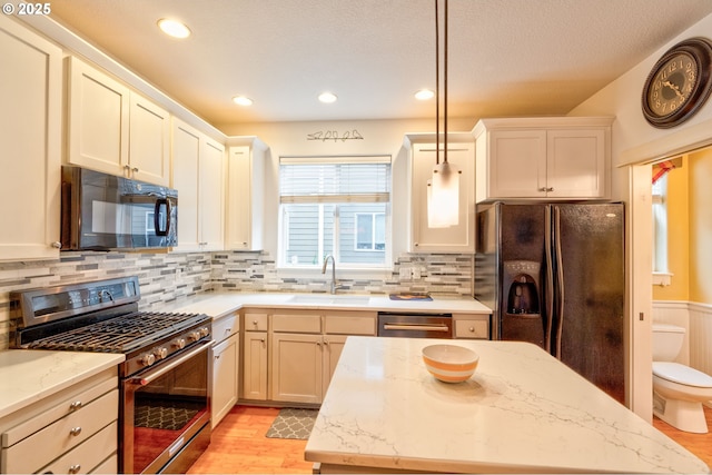 kitchen featuring black appliances, light hardwood / wood-style floors, light stone countertops, pendant lighting, and sink