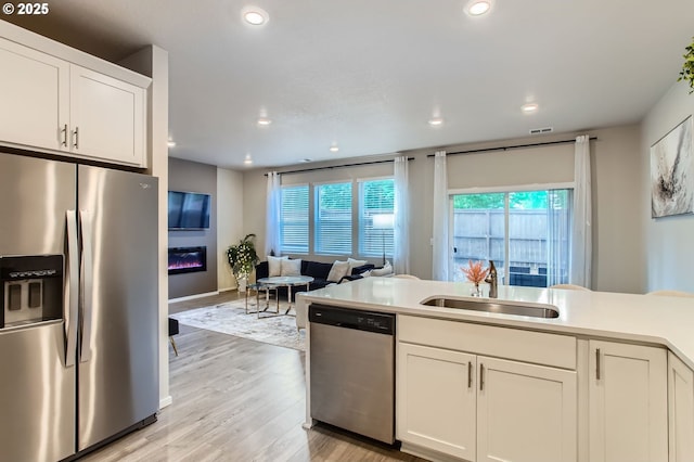 7897 SW Mara Ct, Portland, OR 97224 - kitchen with stainless steel appliances, recessed lighting, a sink, light wood-style floors, and a glass covered fireplace