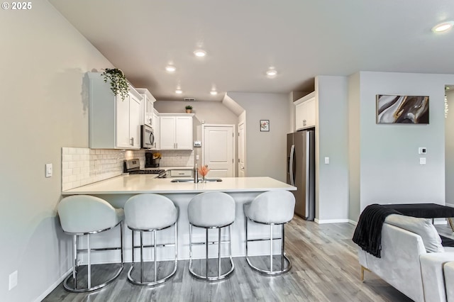 7897 SW Mara Ct, Portland, OR 97224 - kitchen with stainless steel appliances, a peninsula, light wood finished floors, baseboards, and tasteful backsplash