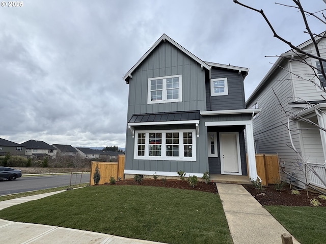 traditional home with board and batten siding, a standing seam roof, fence, and a front lawn