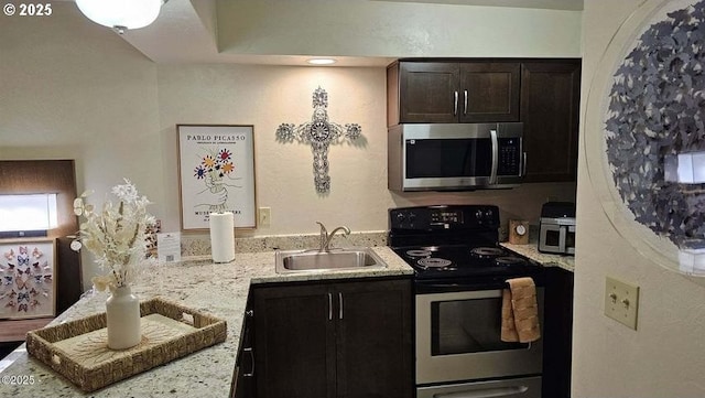 kitchen featuring appliances with stainless steel finishes, a sink, light stone countertops, and dark brown cabinetry