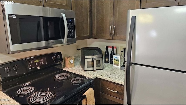 kitchen with freestanding refrigerator, stainless steel microwave, black range with electric stovetop, dark brown cabinets, and light stone countertops