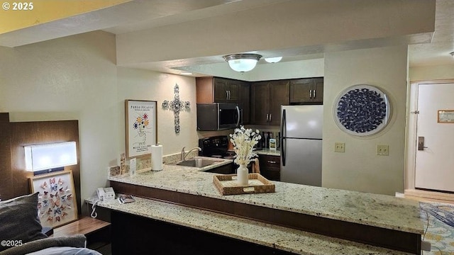 kitchen with stainless steel appliances, a sink, dark brown cabinets, a peninsula, and light stone countertops