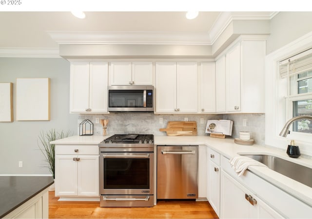 621 NE Randall Ave, Portland, OR 97232 - kitchen featuring appliances with stainless steel finishes, a sink, crown molding, light wood-style flooring, and backsplash