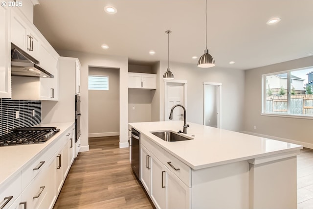 kitchen featuring sink, hanging light fixtures, a kitchen island with sink, white cabinets, and black appliances