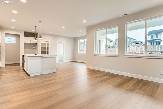 kitchen featuring decorative light fixtures, light wood-type flooring, white cabinetry, and an island with sink