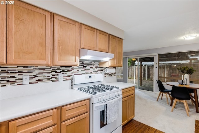 kitchen with dark wood-style floors, white gas range, light countertops, backsplash, and under cabinet range hood