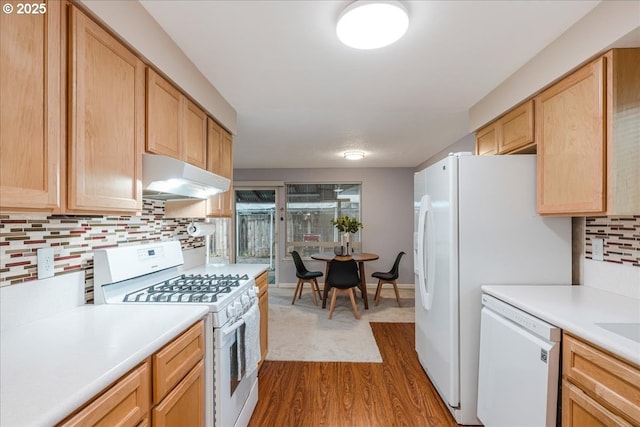 kitchen with white appliances, under cabinet range hood, light countertops, and decorative backsplash