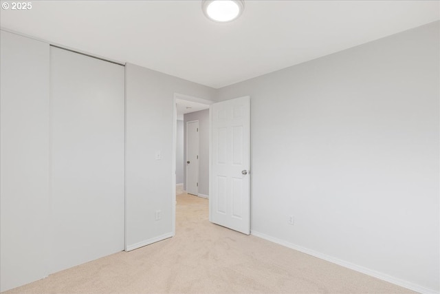 unfurnished bedroom with light carpet, a closet, and baseboards