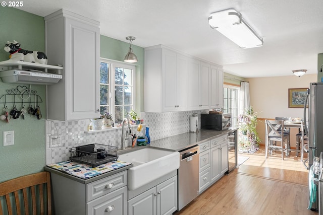 kitchen featuring appliances with stainless steel finishes, backsplash, light wood-type flooring, pendant lighting, and sink