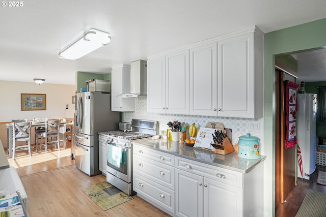 kitchen with white cabinetry, stainless steel appliances, backsplash, light wood-type flooring, and wall chimney exhaust hood