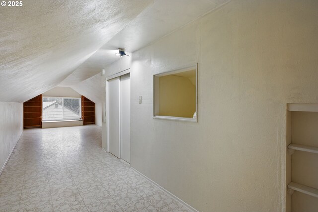 additional living space with tile patterned floors, a textured ceiling, a textured wall, and vaulted ceiling