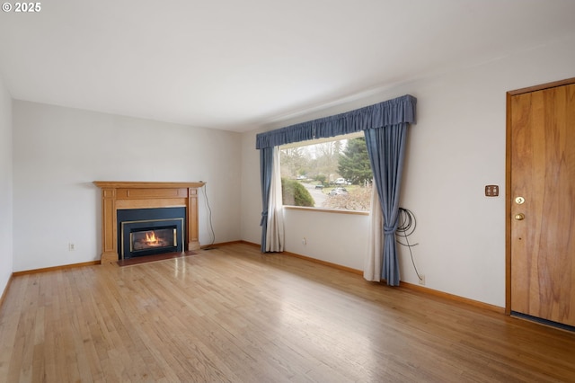 unfurnished living room featuring a glass covered fireplace, light wood-style floors, and baseboards