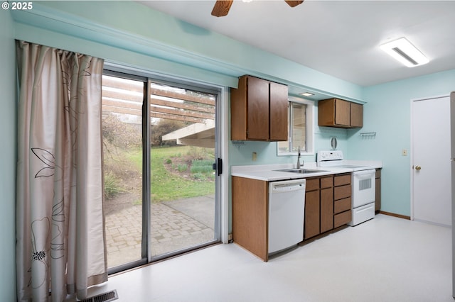 kitchen featuring baseboards, light floors, light countertops, white appliances, and a sink