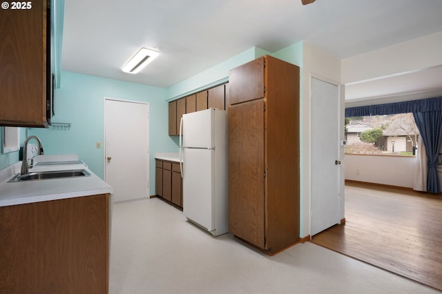 kitchen with light floors, light countertops, brown cabinets, freestanding refrigerator, and a sink