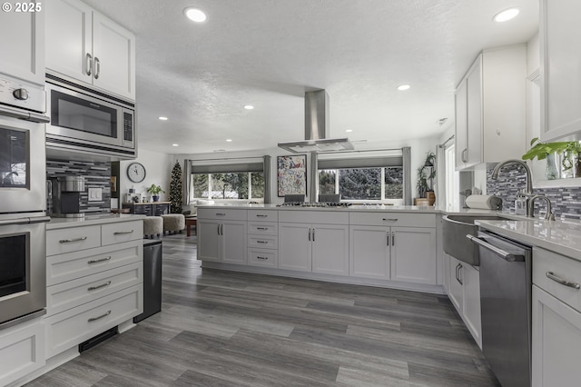 kitchen featuring backsplash, light countertops, island range hood, white cabinets, and stainless steel appliances