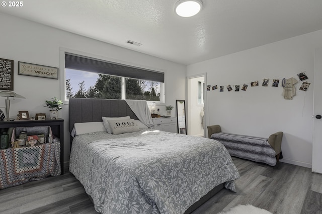 bedroom with visible vents, baseboards, a textured ceiling, and wood finished floors