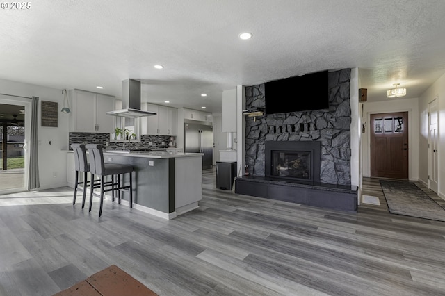 kitchen with built in refrigerator, tasteful backsplash, open floor plan, a breakfast bar area, and wall chimney exhaust hood