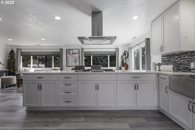 kitchen featuring a textured ceiling, backsplash, dark wood finished floors, island range hood, and stainless steel gas cooktop