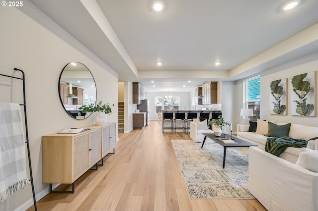 living area featuring stairway, recessed lighting, light wood-style floors, a raised ceiling, and a chandelier