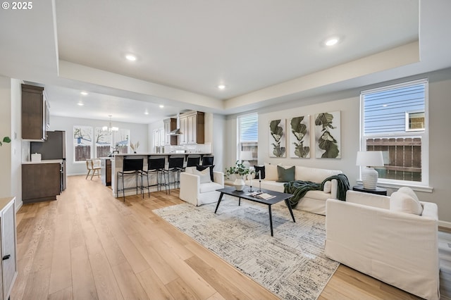 living room featuring a raised ceiling, recessed lighting, light wood-type flooring, and a chandelier