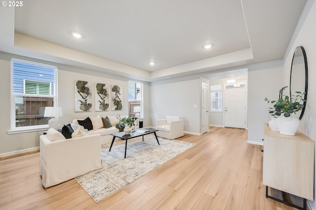 living room with a healthy amount of sunlight, light wood-type flooring, a raised ceiling, and baseboards