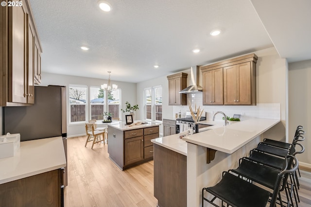 kitchen featuring light wood-style flooring, tasteful backsplash, appliances with stainless steel finishes, a breakfast bar area, and wall chimney range hood