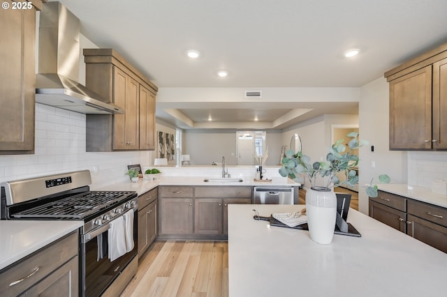 kitchen with a sink, wall chimney range hood, stainless steel appliances, light wood finished floors, and light countertops