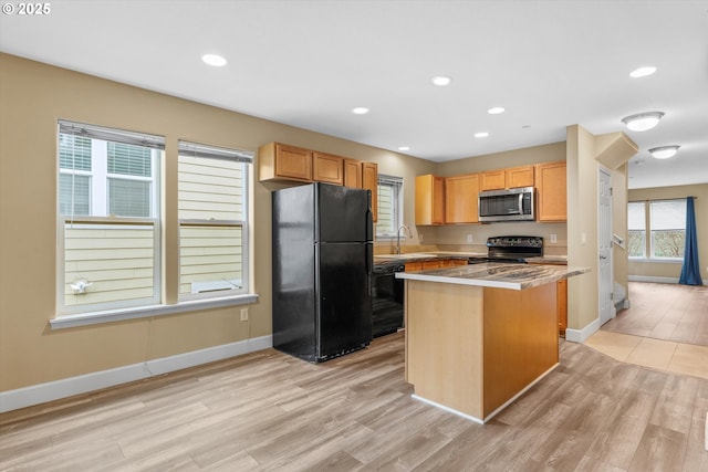 kitchen featuring a center island, a sink, black appliances, light wood-type flooring, and baseboards