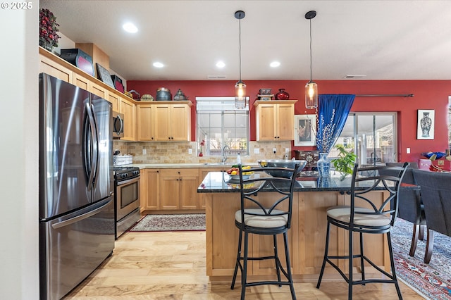 kitchen with a kitchen island, appliances with stainless steel finishes, decorative light fixtures, sink, and a kitchen bar