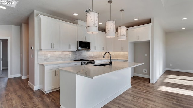 kitchen featuring white cabinetry, sink, hanging light fixtures, stainless steel appliances, and a center island with sink