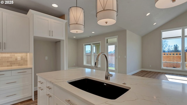 kitchen featuring sink, light stone counters, white cabinetry, and hanging light fixtures