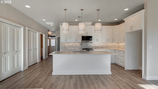 kitchen featuring sink, hanging light fixtures, light hardwood / wood-style floors, a kitchen island with sink, and white cabinets