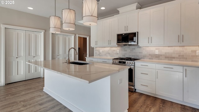 kitchen featuring sink, stainless steel appliances, decorative light fixtures, a center island with sink, and white cabinets