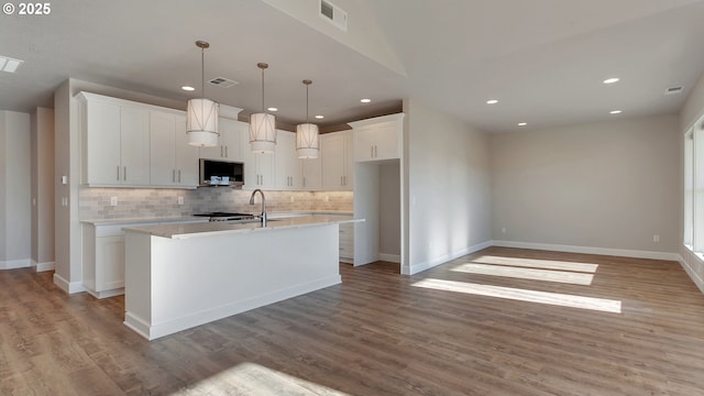 kitchen with pendant lighting, light hardwood / wood-style floors, white cabinetry, and an island with sink