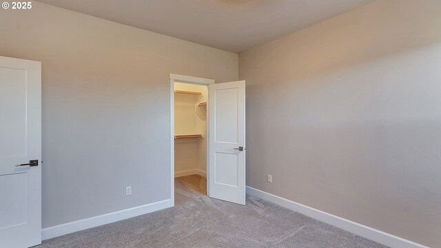 unfurnished bedroom with a spacious closet, light carpet, and a closet