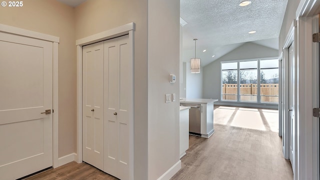 hallway with light wood-type flooring, a textured ceiling, and vaulted ceiling