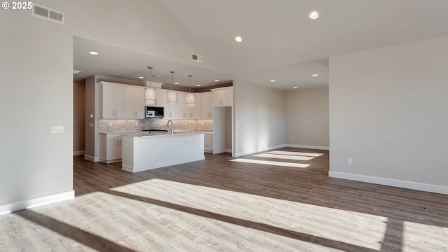 kitchen featuring hardwood / wood-style floors, decorative light fixtures, white cabinetry, and an island with sink