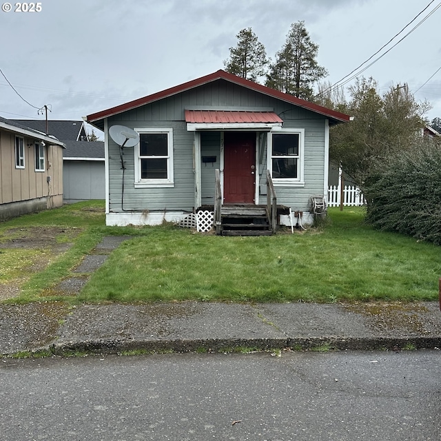 bungalow-style house featuring metal roof, entry steps, a front lawn, and fence