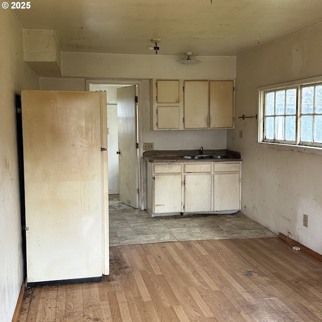 kitchen with dark countertops, cream cabinets, freestanding refrigerator, light wood-style floors, and a sink